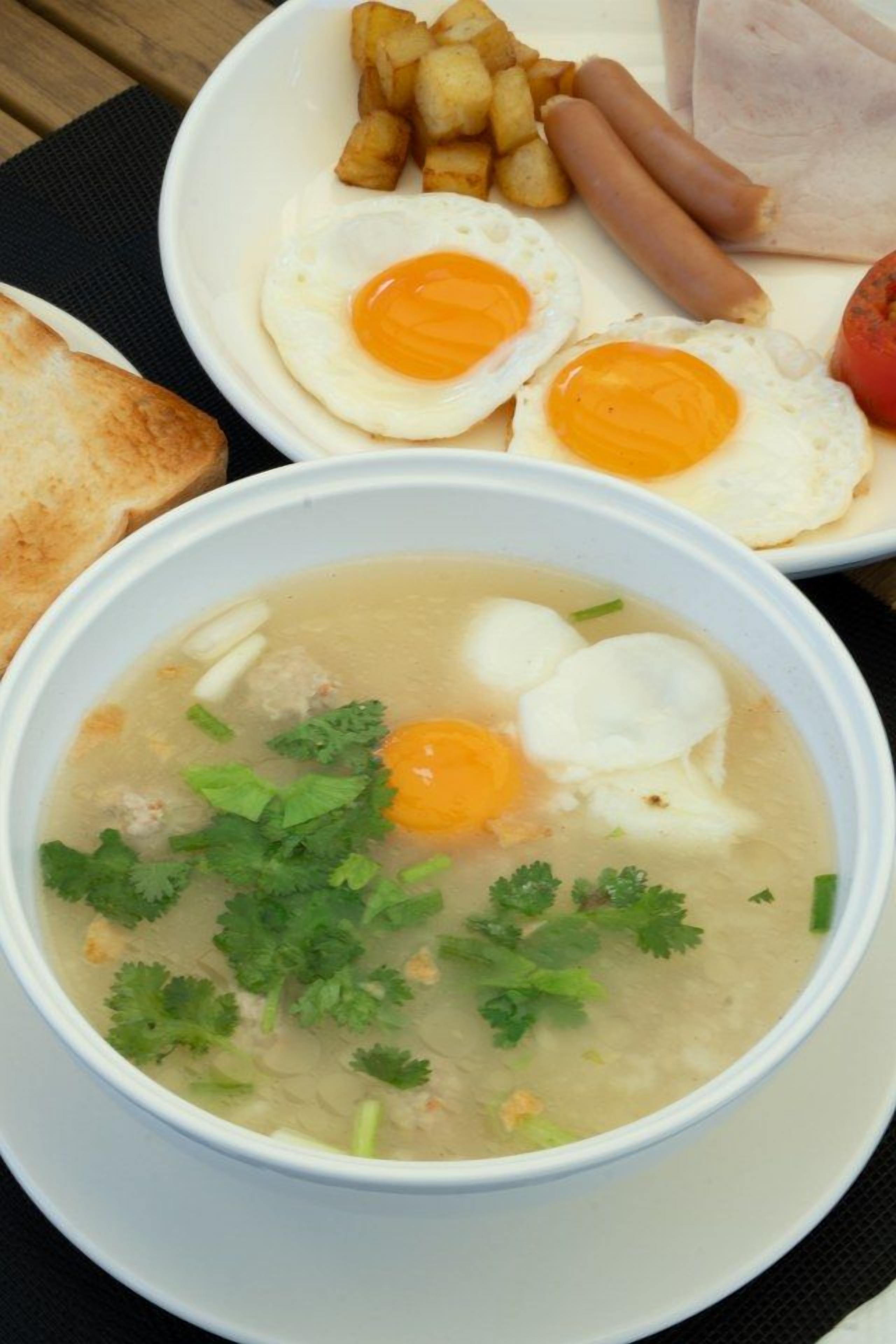 Un plato de sopa con huevos, una fuente de huevos fritos, salchichas y patatas fritas.