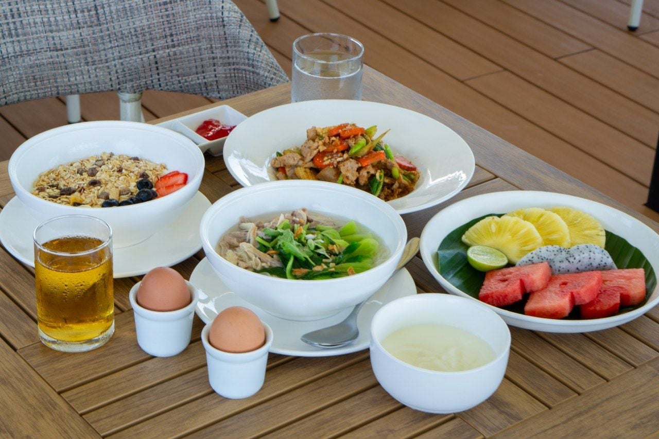 A table with various dishes, including a bowl of soup, a plate of meat and vegetables, a bowl of fruit, and a glass of beer.