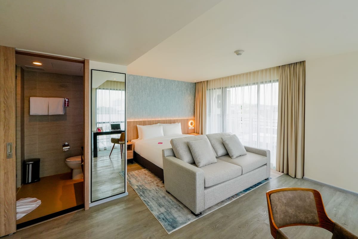 A modern hotel room with a bed, a sofa, a chair, and a bathroom.