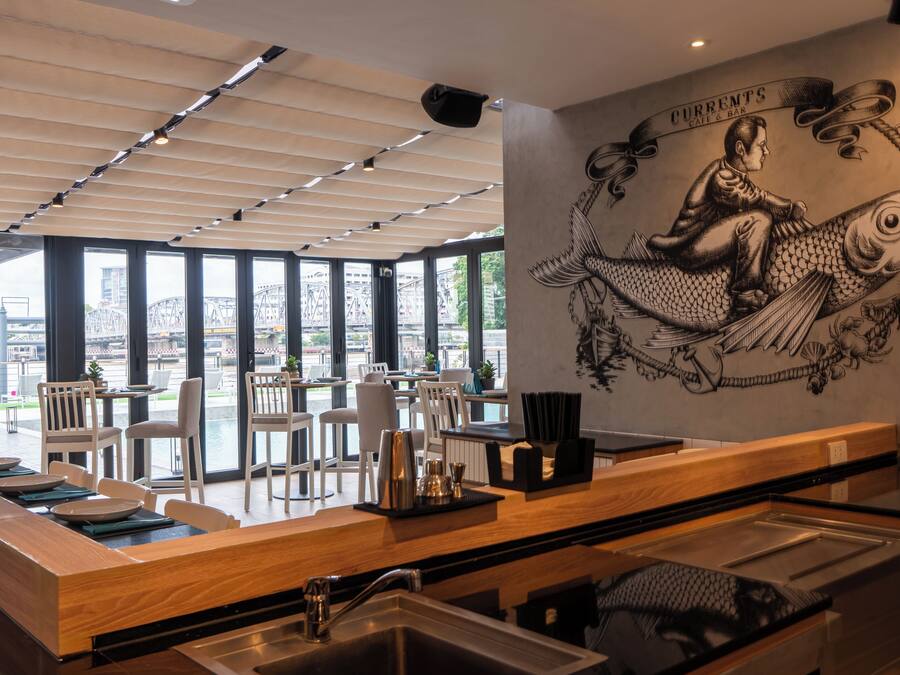 A restaurant with a large mural of a man on a fish, a long counter with chairs, and large windows overlooking a cityscape.