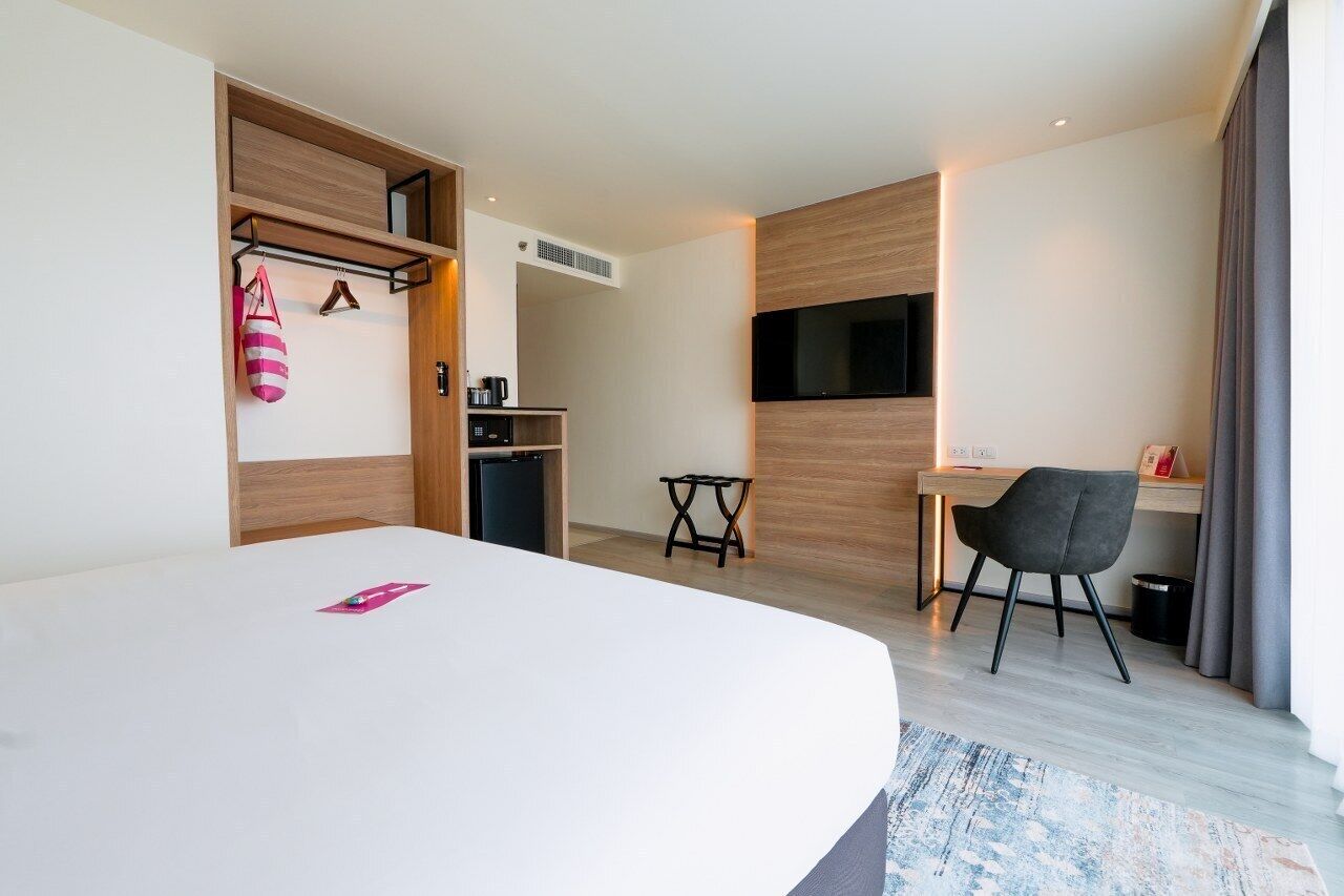 Una habitación de hotel moderna con una cama grande, un escritorio, una silla, un televisor y un armario.