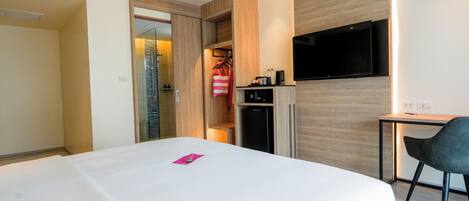 A hotel room with a bed, a desk, a TV, a wardrobe, and a small kitchenette.