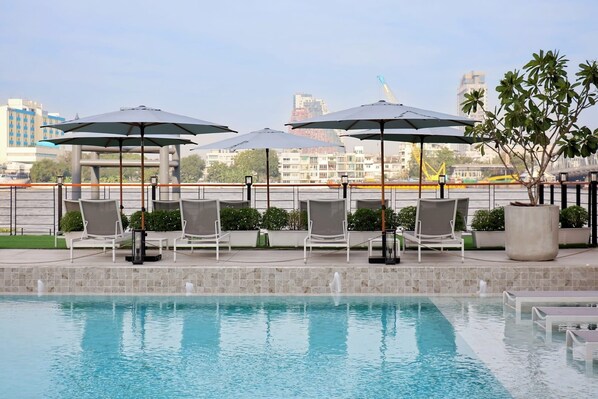 A poolside area with lounge chairs and umbrellas, a view of the cityscape, and a clear sky.