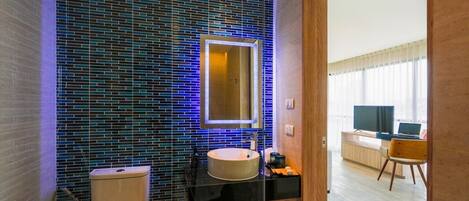 Un baño moderno con pared de azulejos, un lavabo redondo y un inodoro.