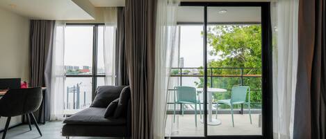 A modern hotel room with a sofa, a desk, and a balcony with chairs.