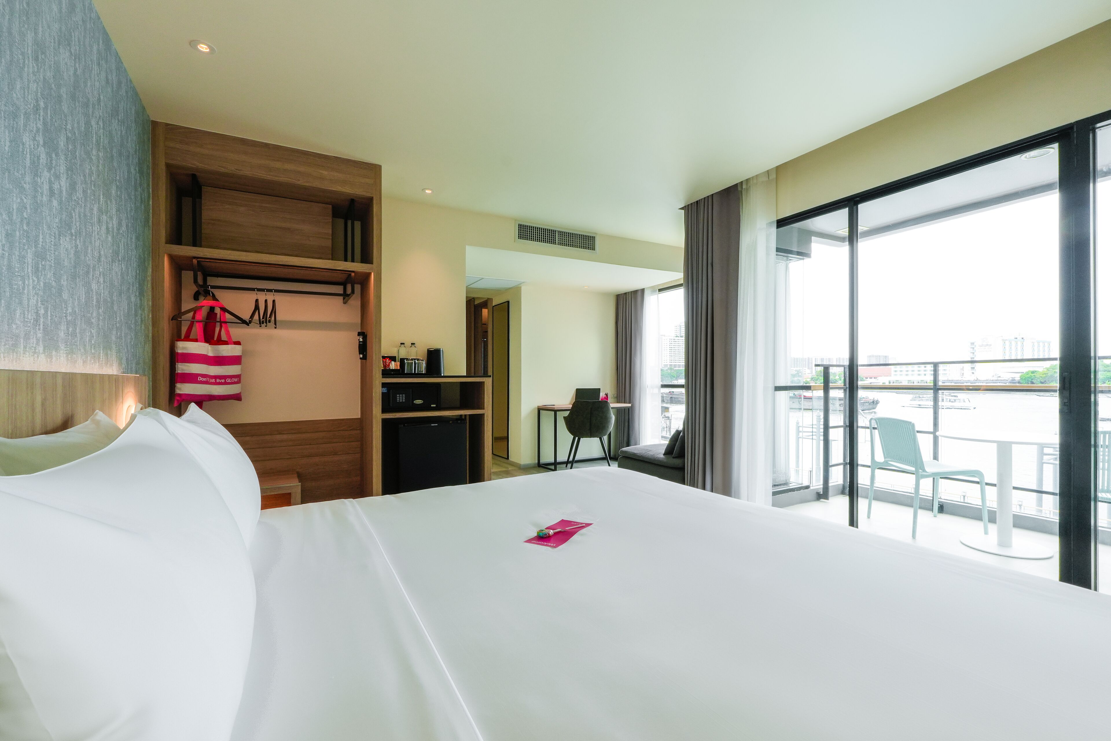 A hotel room with a large bed, a wardrobe, a desk, a chair, and a balcony with a view of the city.