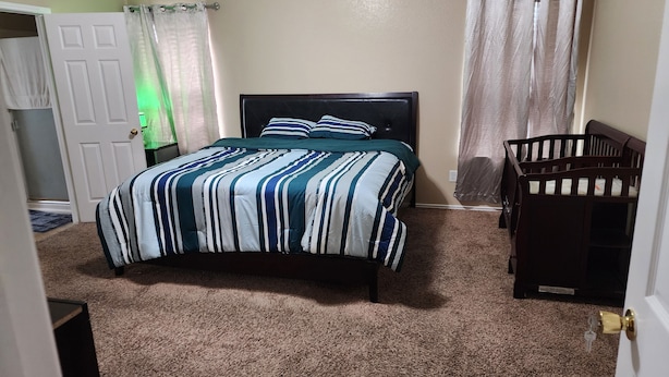 Un dormitorio con una cama, una cuna, paredes color crema y suelo alfombrado.