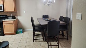 Un comedor con una mesa, sillas, una araña y una zona de cocina con armarios y electrodomésticos.