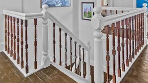 Una escalera de madera con balaustres blancos y barandilla, que conduce a un rellano con techo blanco y una lámpara.