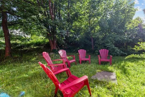 Cuatro sillas Adirondack rojas en un césped con árboles al fondo.