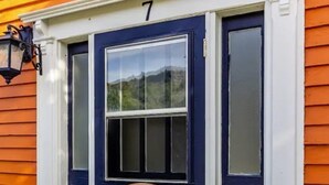 Una puerta azul oscuro con el número blanco "7" encima, una pequeña placa de madera con texto, y un felpudo azul con diseños florales en la entrada.