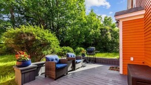 Una terraza de madera con mobiliario exterior y una parrilla.