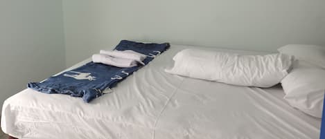 A single bed with white bedding, a blue blanket, and two pillows.