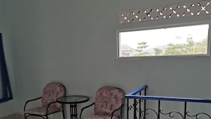 Une chambre avec un balcon, deux chaises, une petite table et une fenêtre donnant sur des arbres et des immeubles.