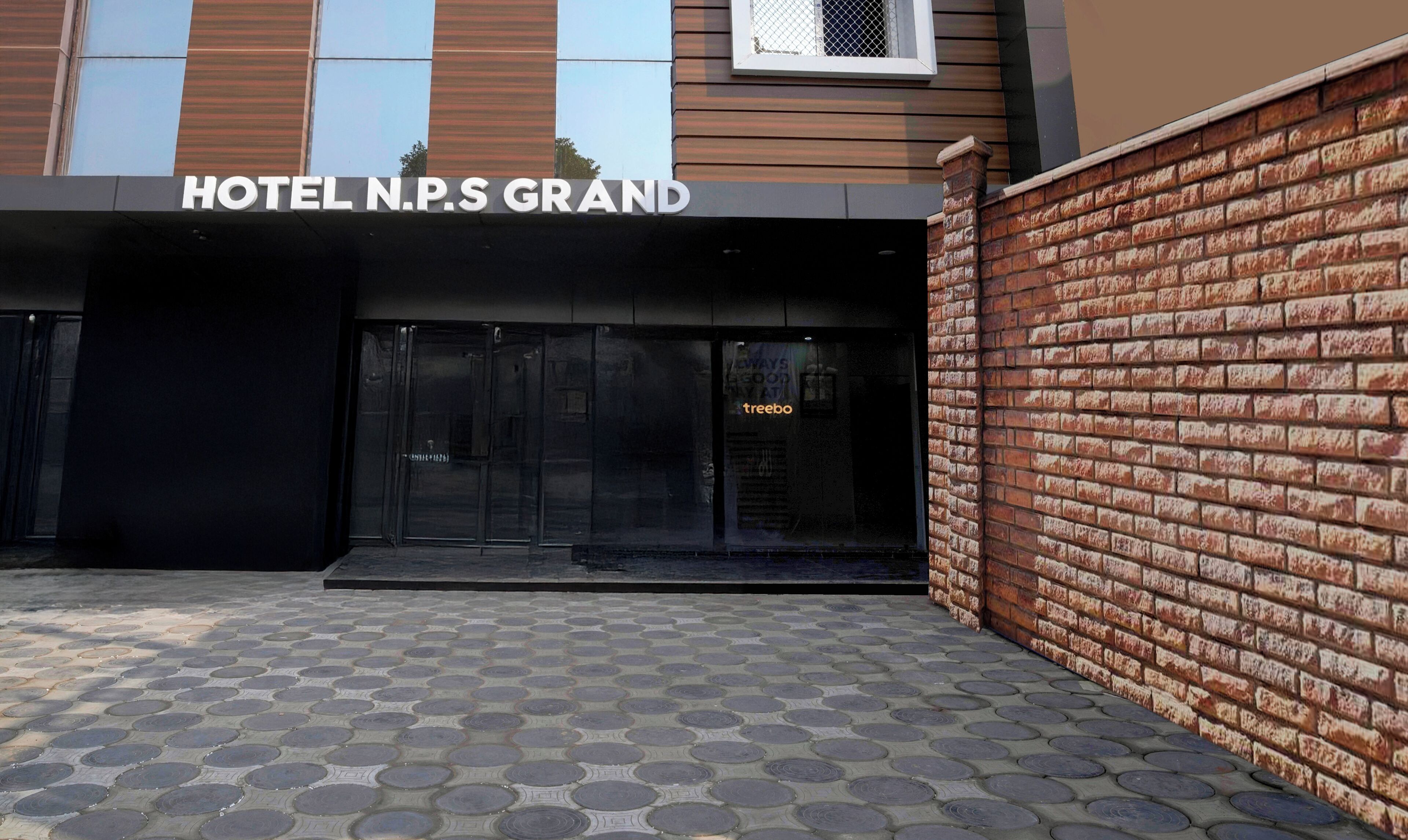 La entrada del HOTEL N.P.S GRAND, con un muro de ladrillo y pavimento de baldosas.