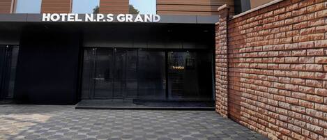 La entrada del HOTEL N.P.S GRAND, con un muro de ladrillo y pavimento de baldosas.