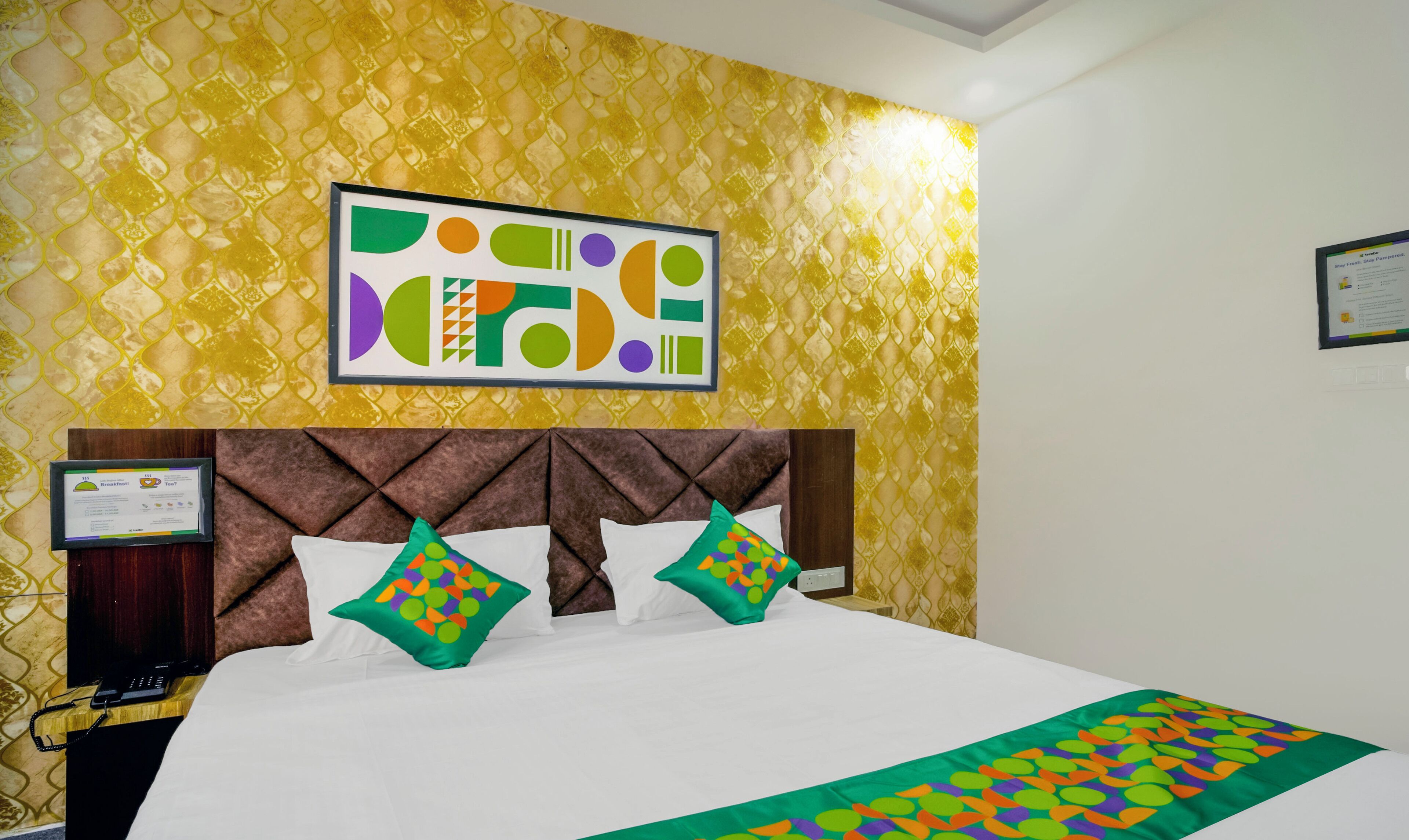 A hotel room with a bed, a headboard, and a wall with a geometric patterned wallpaper.