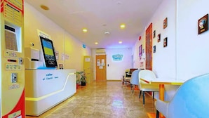 A hotel reception area with a check-in counter, a self-service kiosk, and a seating area with chairs and tables. - Coller Chinatown (Singapore)