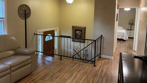 Amplia sala de estar con sofá de cuero, una escalera de madera y un pasillo que conduce a un dormitorio.