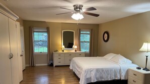 Un dormitorio con cama, mesitas de noche, cómoda, ventilador de techo y ventana con cortinas.