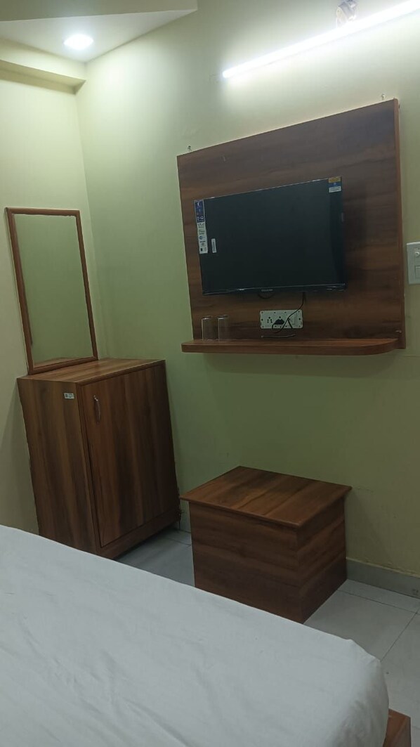 Un dormitorio con cama, cómoda de madera, televisor montado en la pared y un mueble de madera pequeño.