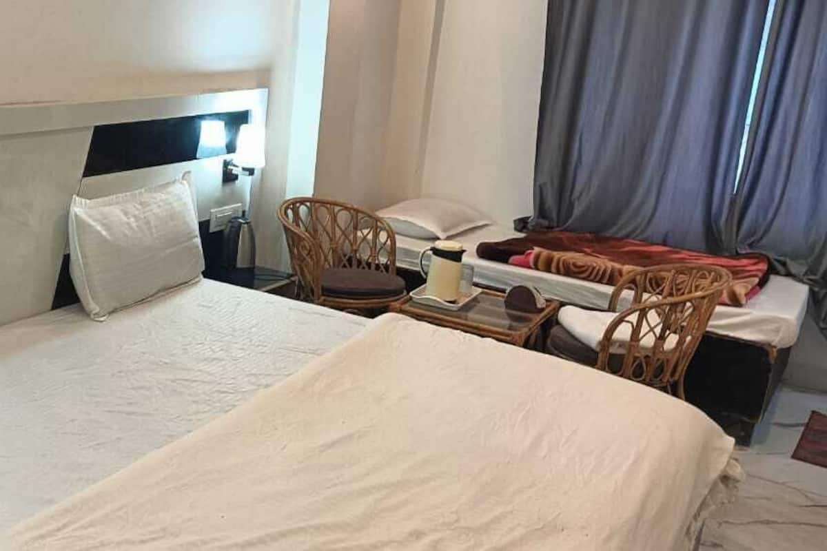 Habitación de hotel con una cama grande, dos almohadas, una mesita de noche con una lámpara, una silla y una pequeña mesa con una taza.