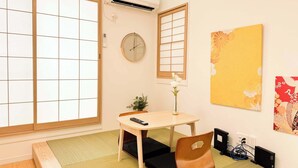 A traditional Japanese room with tatami flooring, a shoji screen, a wooden table, a chair, a clock, and artwork on the walls.