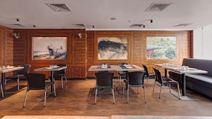 Een moderne eetruimte met houten lambrisering, meerdere tafels en stoelen, en grote ramen met uitzicht op de omgeving.