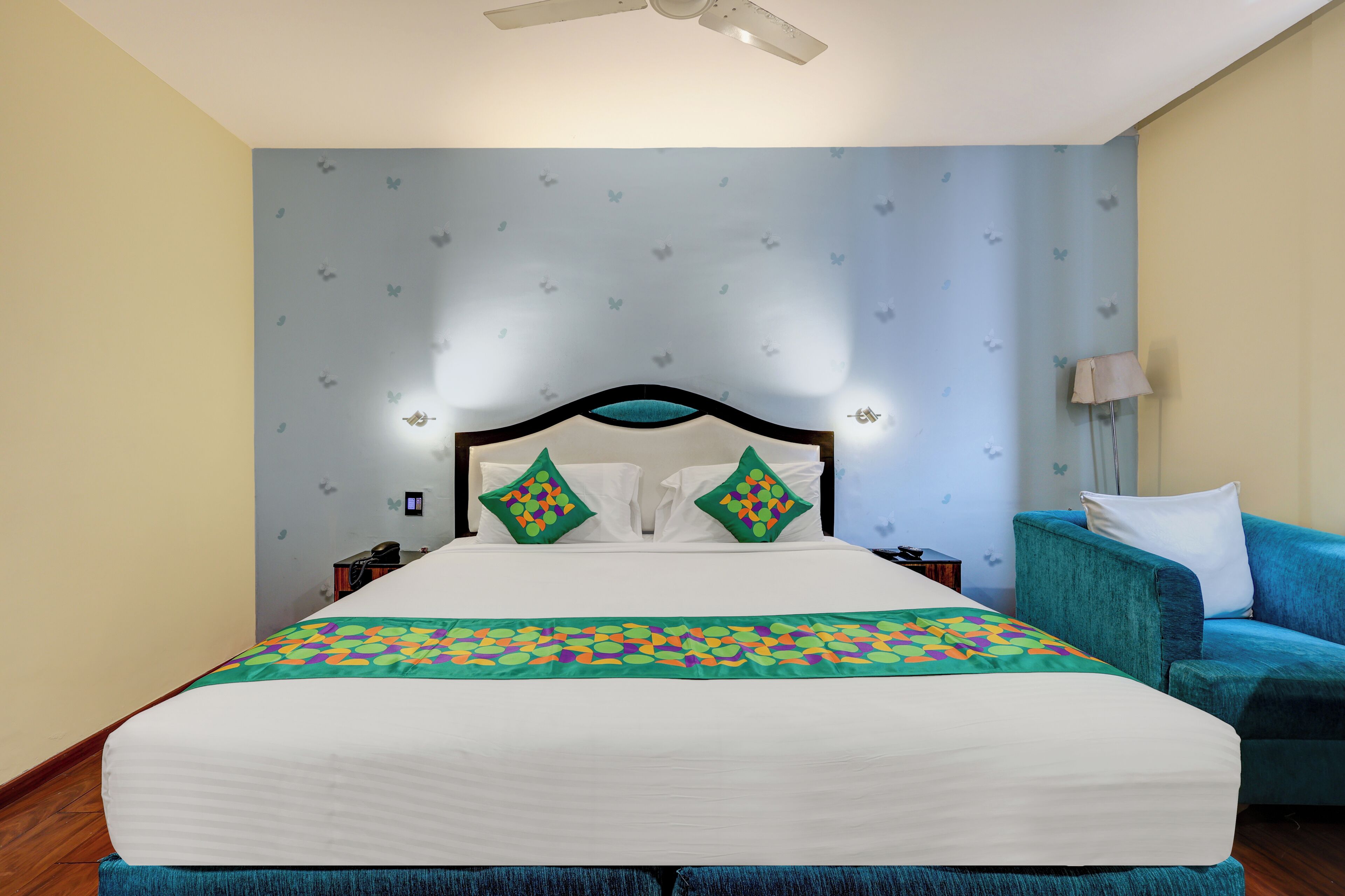 A hotel room with a bed, a blue armchair, a nightstand, and a ceiling fan.