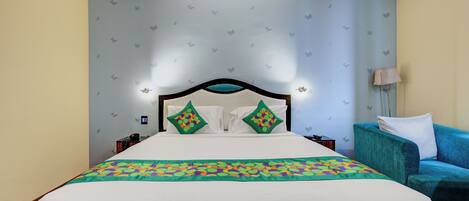 A hotel room with a bed, a blue armchair, a nightstand, and a ceiling fan.