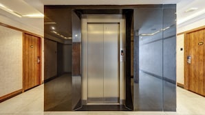 Een moderne lift met een metalen afwerking, omringd door houten deuren en een betegelde vloer.