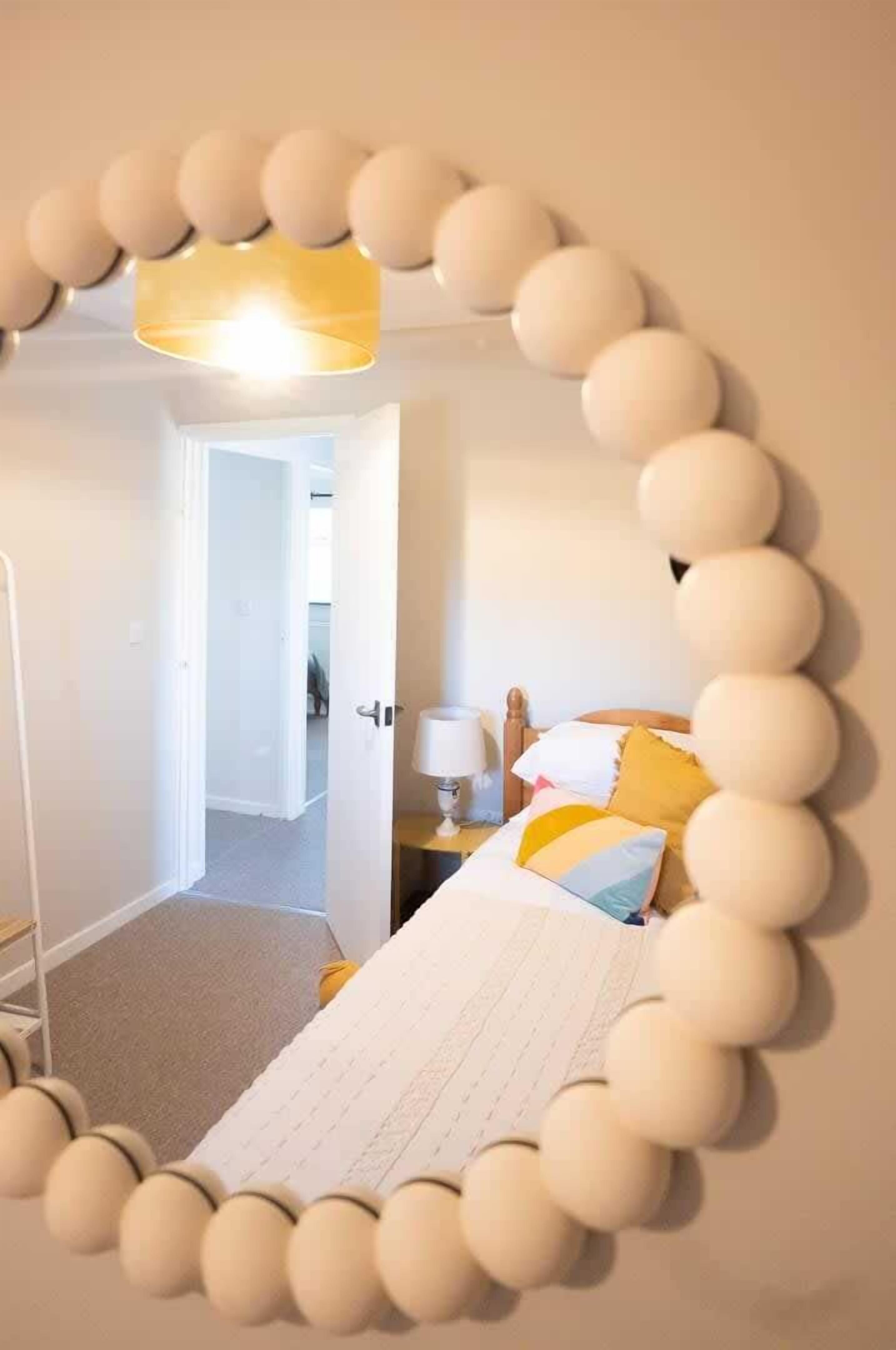 Camera da letto con un letto, un comodino, una lampada e uno specchio con cornice decorativa.