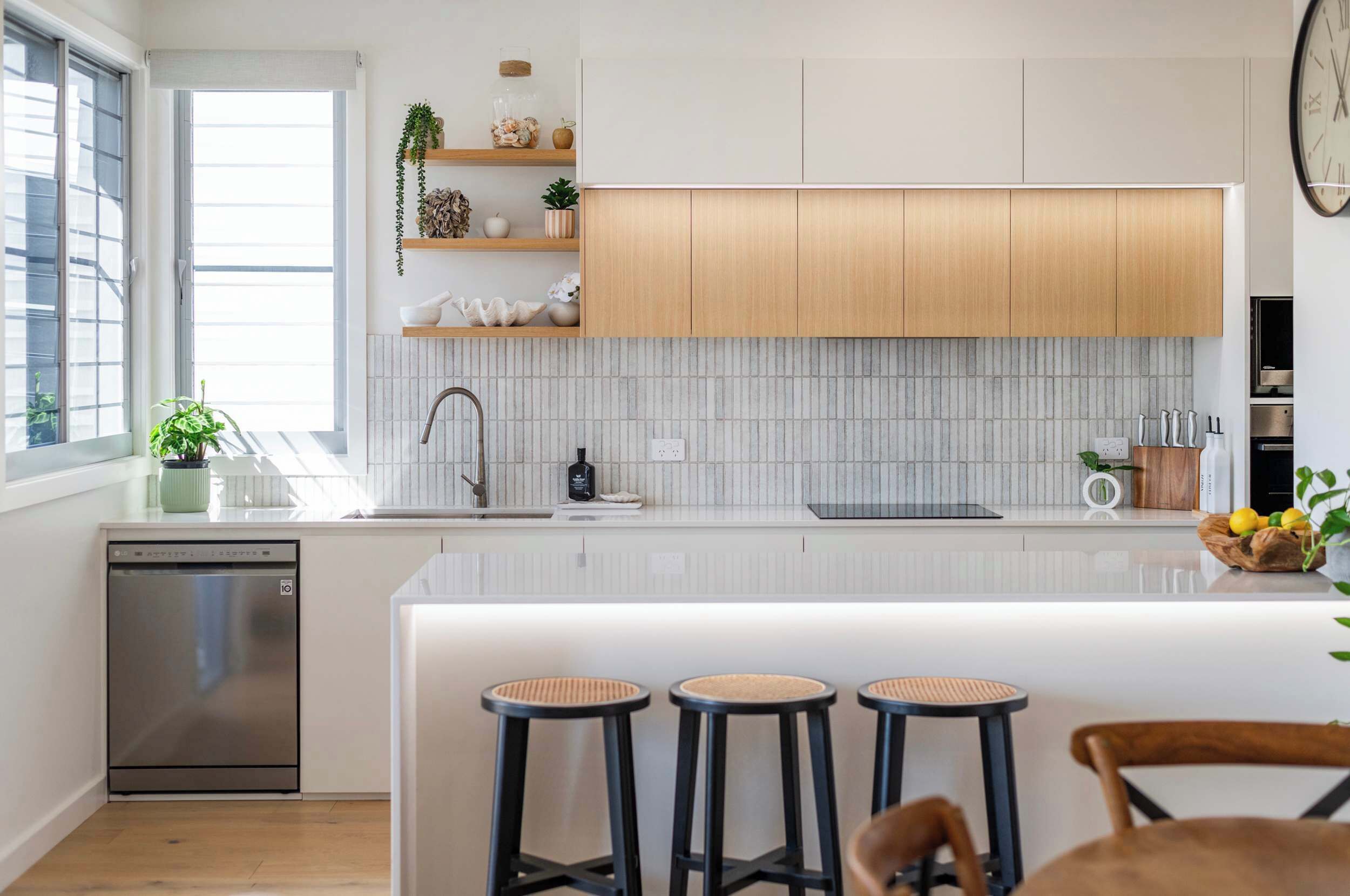 A modern kitchen with white cabinetry, a built-in dishwasher, and a large island with bar stools.