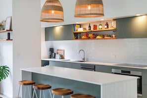 Een moderne keuken met een centraal eiland, barkrukken, hanglampen en inbouwplanken.