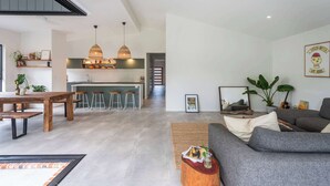 A spacious living area with a grey sofa, wooden dining table, and a kitchen in the background.
