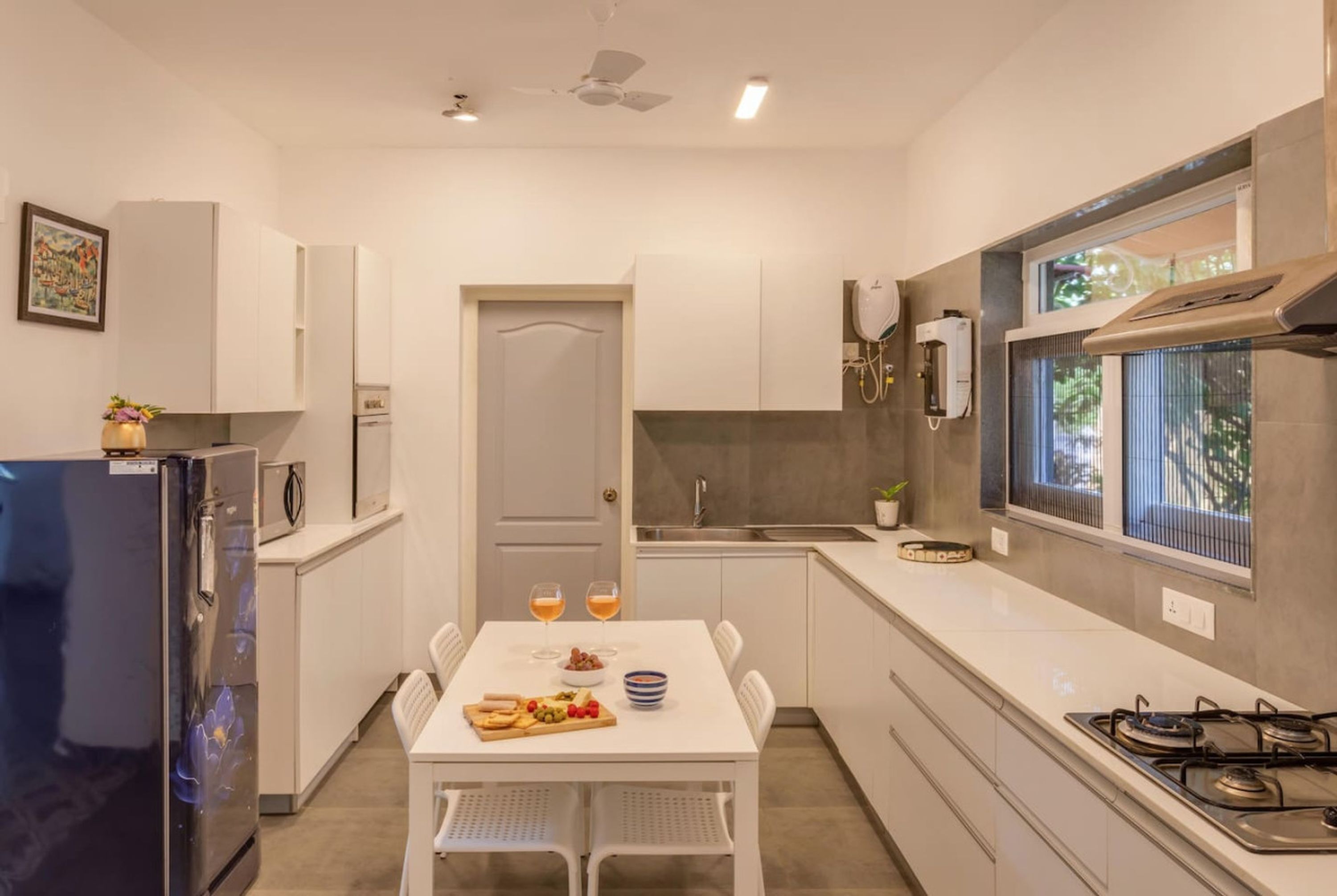 Une cuisine moderne avec des meubles blancs, une cuisinière à gaz, un réfrigérateur et une table à manger dressée avec de la nourriture et des boissons.