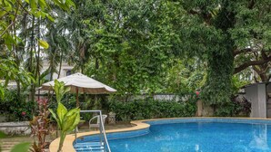 A swimming pool surrounded by lush greenery and a covered seating area. - 4BR Villa With Pool 10 Mins From Calangute Beach (Calangute)