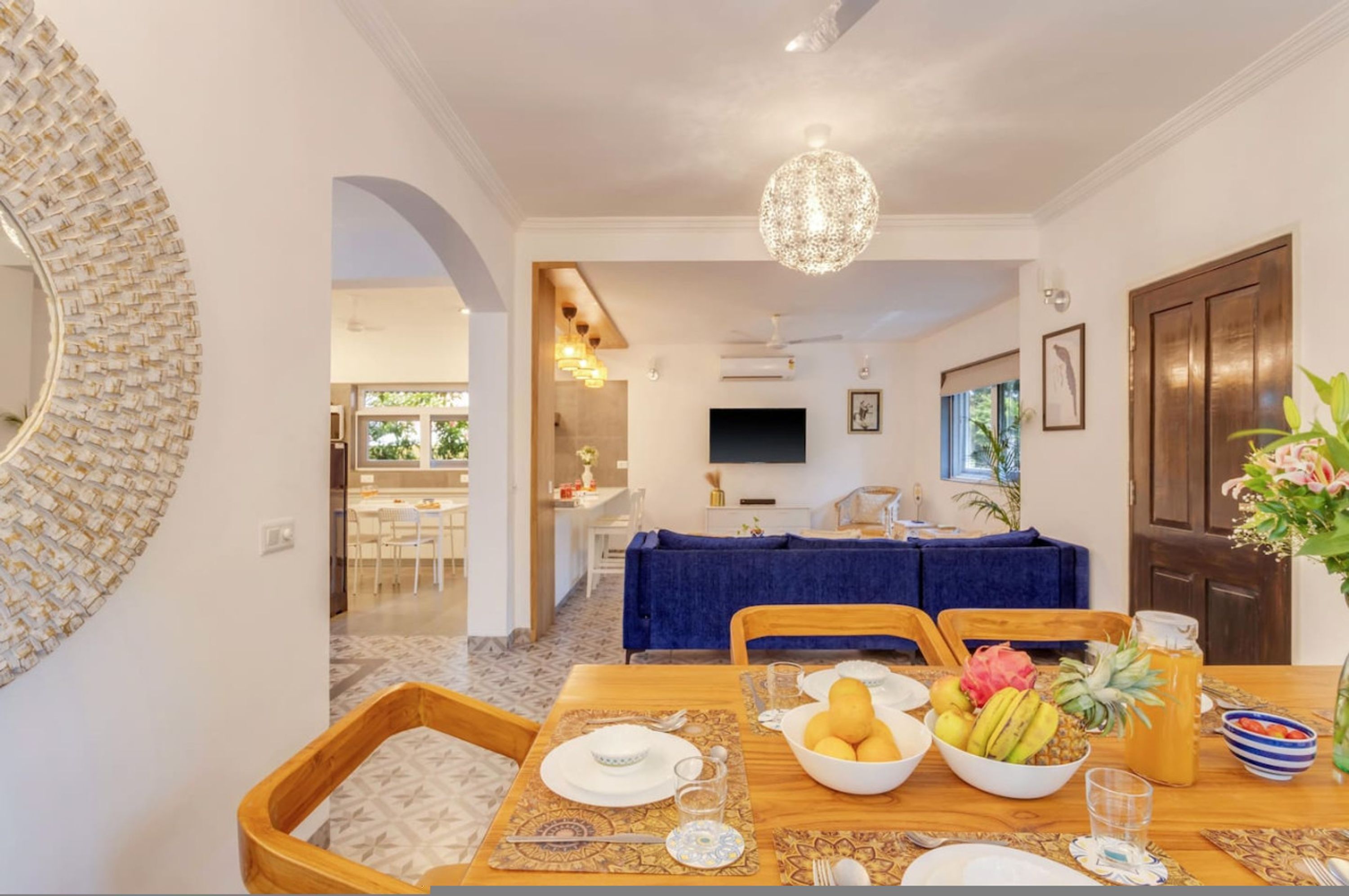A dining area with a table set for four, a television in the background, and a decorative mirror on the wall.