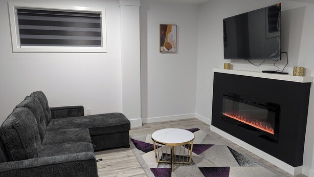 A modern living room with a fireplace, a sofa, a TV, and a patterned rug. - President's Choice: Spacious 1-Bedroom Basement Suite with Fireplace (Edmonton)
