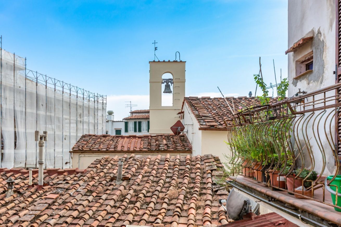A rooftop with terracotta tiles, a bell tower, and potted plants.