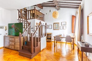 Una habitación amplia con una escalera de madera, un comedor y un cuadro grande.