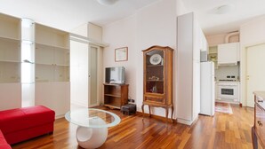 Ein kompakter Wohnbereich mit einem roten Sofa, einem Glastisch, einem Holzschrank und einer Küchenzeile.