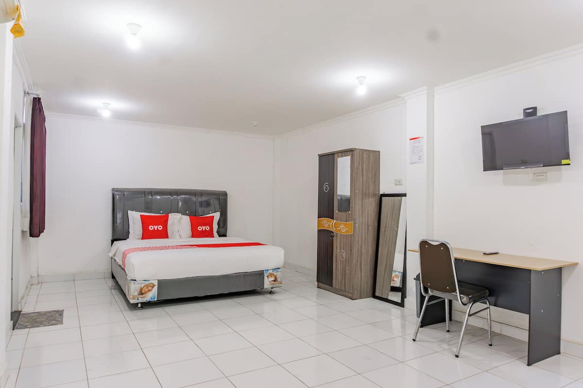 Quarto de hotel com cama, secretária, cadeira, guarda-roupa e televisão.