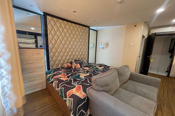 A bedroom with a bed, a grey sofa, a wardrobe, and a mirror. - Hotel O Grand Asia Afrika Apartment By Qr Property (Bandung)