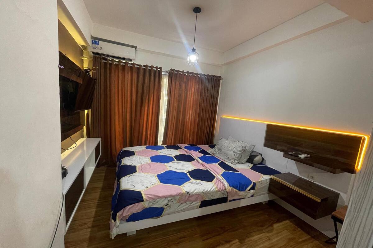 Une chambre à coucher avec un lit, une table de chevet, une télévision et un luminaire au plafond.