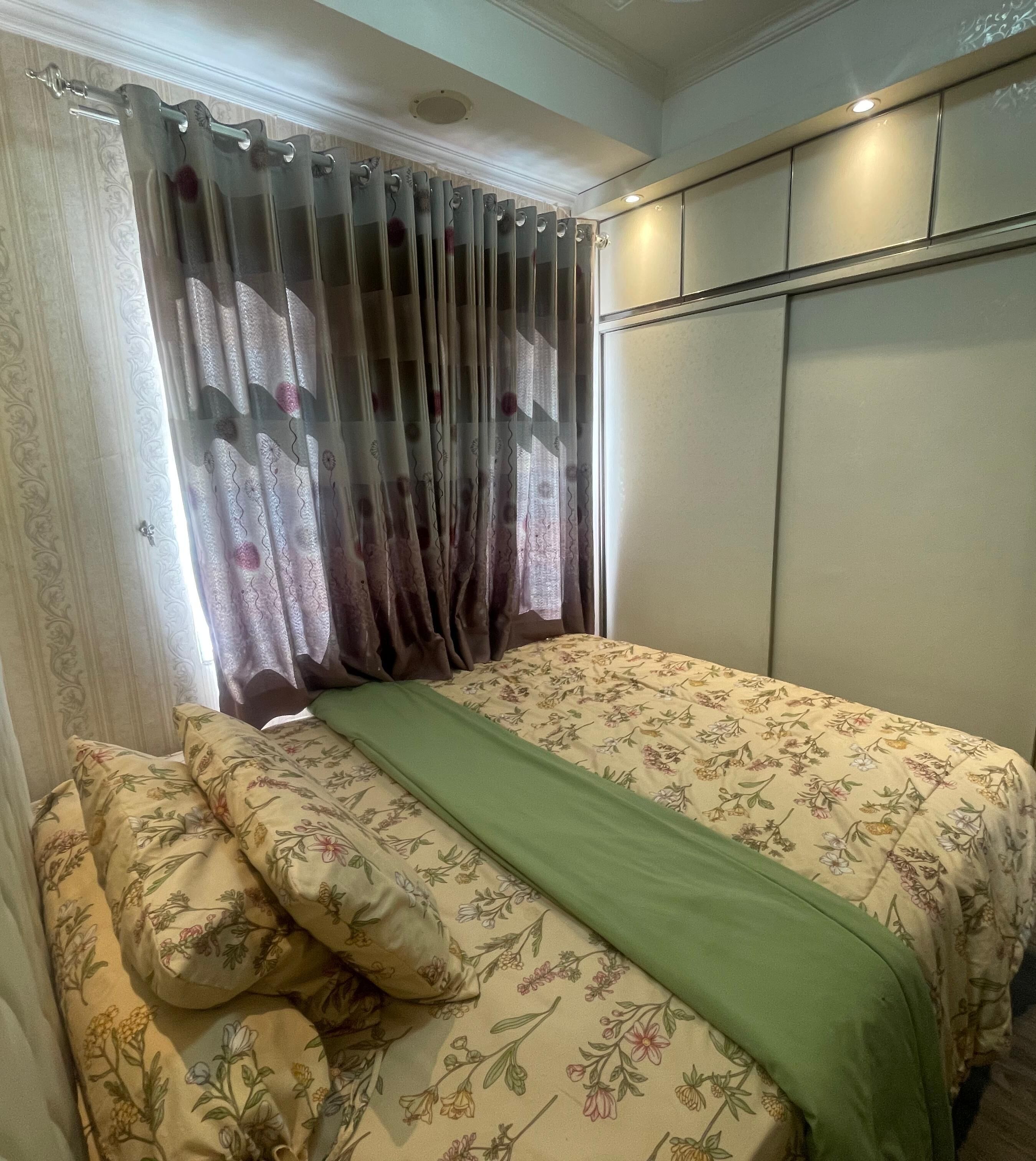 Un dormitorio con cama, ropa de cama estampada, una manta verde y un armario con puertas correderas.