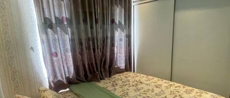 Un dormitorio con cama, ropa de cama estampada, una manta verde y un armario con puertas correderas.