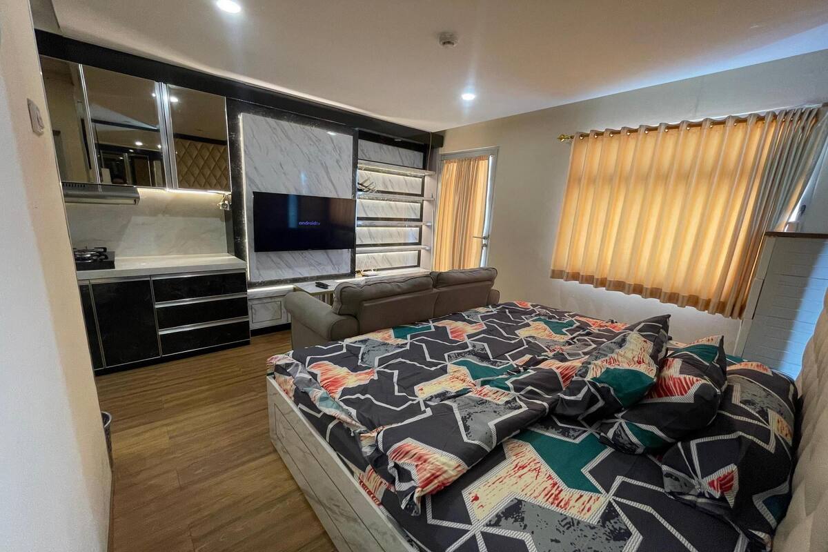 Une chambre moderne avec un grand lit, un téléviseur fixé au mur, un canapé et un coin cuisine intégré.
