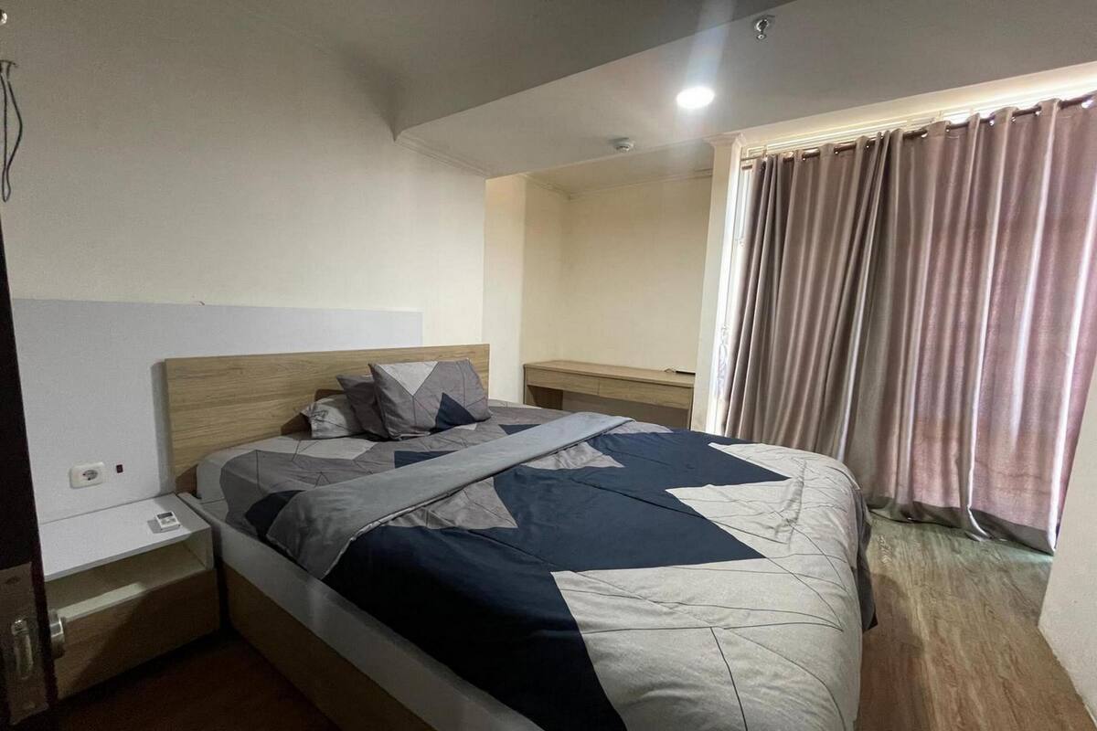 Une chambre d’hôtel comprenant un lit, des tables de chevet, une commode, une fenêtre avec des rideaux et un luminaire au plafond.