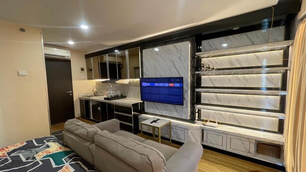 A modern hotel room with a large bed, a sofa, a TV mounted on a marble wall, and a minibar. - Hotel O Grand Asia Afrika Apartment By Qr Property (Bandung)